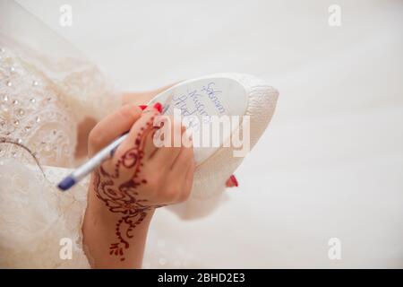 Braut schreibt unter Schuh Hochzeit Ritual Aberglauben. Hand einer Braut schriftlich Single Freunde Namen unter ihrem Schuh vor der Hochzeit. Braut schreibt ihr Stockfoto