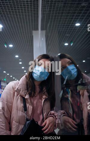 Mädchen allein in medizinischen Maske spiegelt sich im Glas Stockfoto