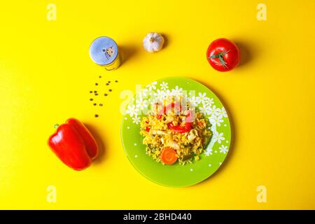 Paella mit Tintenfisch: Traditionelles spanisches Gericht mit Gewürzen und Gemüse auf gelbem Hintergrund. Stockfoto