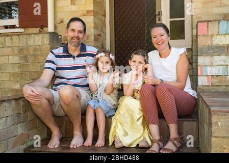 Eine lächelnde simbabwische Familie, die in Australien lebt, sitzt während der Covid-19-Epidemie an der Vordertreppe ihres Hauses in Sydney. Stockfoto