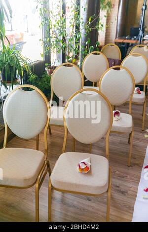 Cremeweiße Hochzeitsstühle im Restaurant. Rosenblätter auf dem Boden. Stockfoto