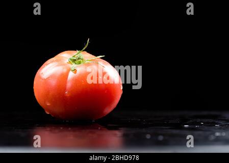 Rote, frische, reife Tomate auf einer schwarzen und nassen Oberfläche. Isoliert in Schwarz. Nahaufnahme Makroaufnahme. Stockfoto