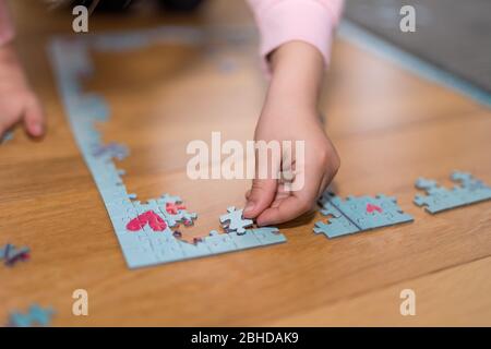 Blonde Mädchen in einem rosa Pullover mit einem Puzzle auf dem Boden durch die Einengung von Coronavirus covid-19 spielen Stockfoto