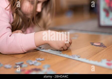 Blonde Mädchen in einem rosa Pullover mit einem Puzzle auf dem Boden durch die Einengung von Coronavirus covid-19 spielen Stockfoto