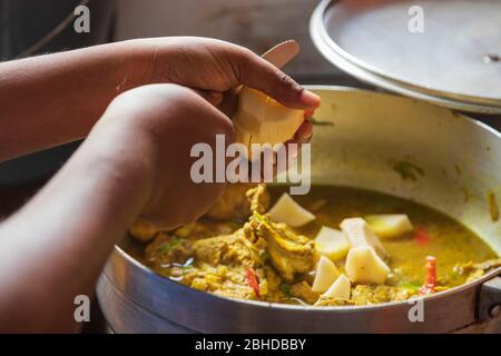 Schneiden von irischen Kartoffeln, um ein geschmortes Curry Huhn und Irish Kartoffelsauce mit roten Paprika indischen Hauskost herrlich zu machen Stockfoto