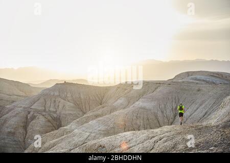 Runner Athlet mit Rucksack auf dem wilden Spur am Berge in der Wüste bei Sonnenuntergang Stockfoto