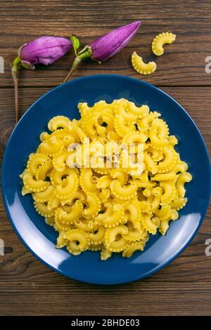 Pene Lisce Pasta in blauer Platte mit Magnolienblüten auf dunklem Holzhintergrund. Von oben Stockfoto