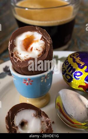 Frohe Ostern. Nahaufnahme eines Cadbury's Creme Egg, das einem gekochten Ei in einer Eierschale ähnelt, zusammen mit einem Espresso-Kaffee zum Frühstück Stockfoto