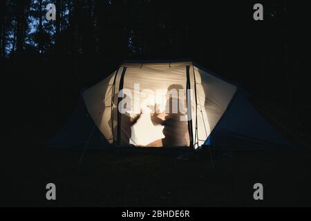 Silhouetten von Kindern, die nachts im Zelt spielen, machen Schattenpuppen mit Taschenlampe und genießen Sommerferien Stockfoto