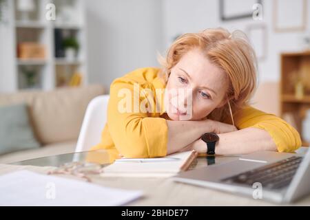 Müde oder nachdenklich reife blonde Geschäftsfrau auf dem Schreibtisch vor dem Laptop liegend während einer kurzen Pause mitten im Arbeitstag Stockfoto