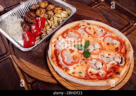 Bratkartoffeln mit gegrilltem Gemüse und Fleisch auf Backblech und Pizza auf Holzhintergrund als Studioaufnahme Stockfoto