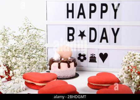 Happy Name Day Leuchtkasten Aufschrift plus Mini-Kuchen tropfenden Dessert. Frühling Blumen und einfache saubere Hintergrund. Makronen rot Herz geformt Stockfoto