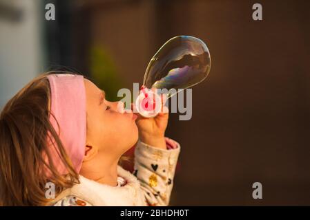 Nettes, kleines Mädchen bläst Seifenblasen vor dunklem Hintergrund Stockfoto