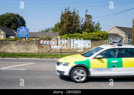 Chippenham, Wiltshire, Großbritannien, 25. April 2020. Ein Medvivo Mobile Care Response-Auto wird abgebildet, als es an einem Schild mit dem Titel „Danke NHS“ vorbeifährt, das an einer Schulwand gegenüber dem Chippenham Community Hospital aufgehängt wurde. Medvivo bietet außerhalb der Geschäftszeiten medizinische Versorgung für Patienten, die in den klinischen Commissioning-Gebieten Bath und North East Somerset, Swindon und Wiltshire bei einem Hausarzt registriert sind. Kredit: Lynchpics/Alamy Live News Stockfoto