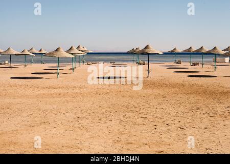 Leerer Strand zur Sommerzeit. Leere passende Sonnenschirme am Strand, blauer Himmel in der Ferne. Horizontal mit Kopierbereich. Stockfoto
