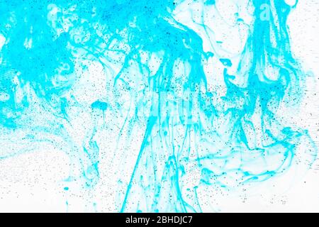 Luftblasen auf der Glasoberfläche der flachen Flasche und der aquamarinfarbenen Tinte fließen im Wasser auf dem Hintergrund Stockfoto