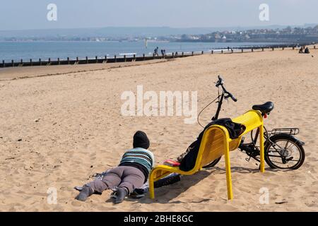 Portobello, Schottland, Großbritannien. 25. April 2020. Blick auf die Menschen im Freien am Samstagnachmittag am Strand und an der Promenade in Portobello, Edinburgh. Gutes Wetter hat mehr Menschen ins Freie gebracht, die wandern und Radfahren. Die Polizei patrouilliert in Fahrzeugen, hält aber nicht an, weil die meisten Menschen soziale Distanzierungen zu beobachten scheinen. Frau, die sich am Strand beim Lesen eines Buchbuches entspannt. Iain Masterton/Alamy Live News Stockfoto