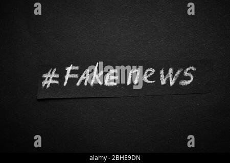 Fake News. Der Name ist in weißer Kreide auf schwarzem Hintergrund in Form von Papier geschrieben. Stockfoto