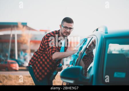 Porträt eines zufriedenen jungen Mannes, der sein eigenes Auto mit einem Tuch putzt. Stockfoto
