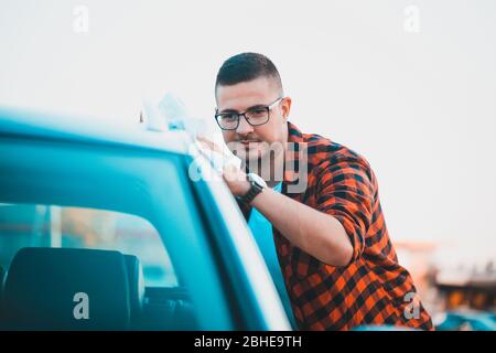 Junger Mann reinigt sein Auto sorgfältig mit Mikrofasertuch. Stockfoto