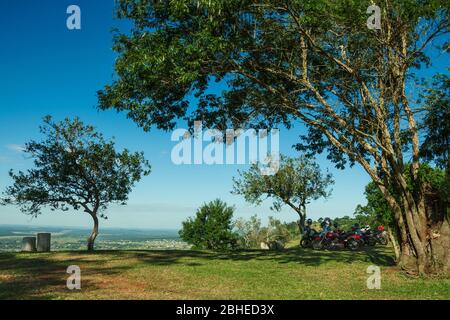 Mehrere geparkte Motorräder unter Bäumen Schatten, auf Hügel von grünen Wiese und sonnigen Tag in der Nähe von Pardinho bedeckt. Ein kleines Dorf auf dem Land Stockfoto