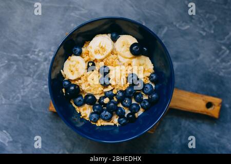 Dunkelblaue Schale Haferbrei Haferbrei mit Banane und Heidelbeere auf Vintage-Tischansicht im flachen Lay-Stil. Warmes Frühstück und hausgemachte Speisen. Stockfoto