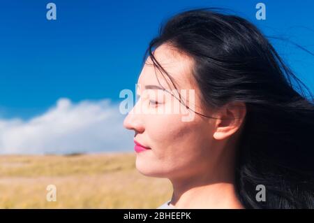 Eine chinesische Frau mit Haaren, die im Wind in der landschaftlich schönen Gegend am Kap Cod Massachusetts an einem sonnigen blauen Himmel weht. Stockfoto