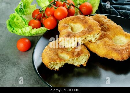 In Scheiben geschnittenes und ganzes navajo Fladenbrot mit Tomaten Kirsche und Salat auf dem schwarzen Hintergrund. Traditionelles indisches navajo Fladenbrot. Stockfoto