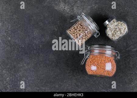 Verschiedene rohe Getreide, Körner für gesundes Kochen in Gläsern auf dunklem Schiefertisch, Hintergrund. Clean Eating, veganes, ausgewogenes Ernährungskonzept Stockfoto