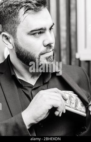 Junger Mann mit Bart, der Dollar Geld in die Tasche legt Stockfoto