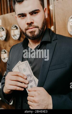 Junger Mann mit Bart, der Dollar Geld in die Tasche legt Stockfoto