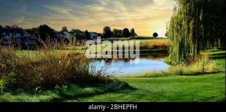 Friedlicher Blick auf einen Golfplatz bei Sonnenuntergang mit Blick auf einen kleinen See mit einem Regenbogen am Himmel. Stockfoto