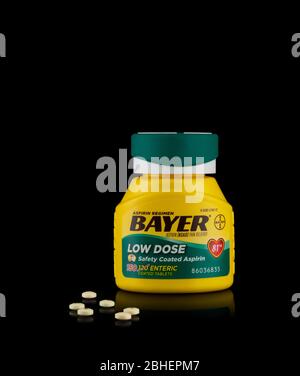Illustratives Editorial von Bayer-Aspirin-Flaschen und Tabletten mit niedriger Dosis auf schwarzem reflektierendem Hintergrund. Stockfoto