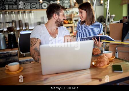 Ein junges Paar, das sich unterhielt und lächelte, und das Frühstück im Coffeeshop hatte, der gerade eröffnet werden sollte. Geschäftskonzept wird gestartet Stockfoto