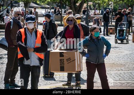 25. April 2020, Hessen, Frankfurt/Main: Demonstranten stehen auf dem Gelände eines Luxushotels in einer Reihe, jeweils zwei Meter voneinander entfernt, mit Koffern und Umzugskartons vor der Alten Oper. Zum Thema "Flüchtlinge und Wohnungsmangel in der Corona-Krise" fanden vor zwei Hotels und einer Jugendherberge Aktionen statt. Foto: Frank Rumpenhorst/dpa Stockfoto