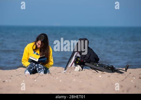 Portobello, Schottland, Großbritannien. 25. April 2020. Blick auf die Menschen im Freien am Samstagnachmittag am Strand und an der Promenade in Portobello, Edinburgh. Gutes Wetter hat mehr Menschen ins Freie gebracht, die wandern und Radfahren. Der Strand scheint voll mit möglicherweise einem Zusammenbruch der sozialen Distanz, die später am Nachmittag stattfindet. Einsame Frau, die am Strand Buch liest. Iain Masterton/Alamy Live News Stockfoto