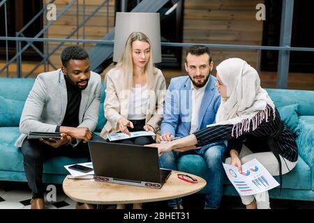 Nahaufnahme von vier intelligenten jungen multirassischen Geschäftspartnern, zwei Männern und zwei Frauen, Brainstorming miteinander, Diskussion über Ideen und Geschäft Stockfoto