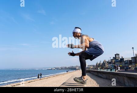 Portobello, Schottland, Großbritannien. 25. April 2020. Blick auf die Menschen im Freien am Samstagnachmittag am Strand und an der Promenade in Portobello, Edinburgh. Gutes Wetter hat mehr Menschen ins Freie gebracht, die wandern und Radfahren. Die Polizei patrouilliert in Fahrzeugen, hält aber nicht an, weil die meisten Menschen soziale Distanzierungen zu beobachten scheinen. Ludovic, Spa Manager und gebürtiger Mauritius, trainiert auf der Promenade. Iain Masterton/Alamy Live News Stockfoto