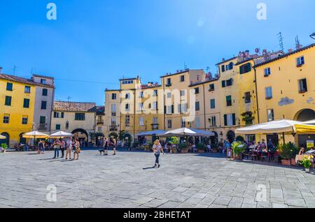 Lucca, Italien, 14. September 2018: Piazza dell Anfiteatro Platz in Zirkushof der mittelalterlichen Stadt historischen Zentrum, alte bunte Gebäude mit und blauen klaren Himmel kopieren Raum Hintergrund, Toskana Stockfoto