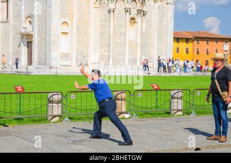 Pisa, Italien, 14. September 2018: Touristen Reisenden kaukasischen und asiatischen chinesen, japanische Männer posieren, Spaß haben, stereotype Fotos machen, vorgeben, berühmten Schiefen Turm, Toskana zu halten Stockfoto