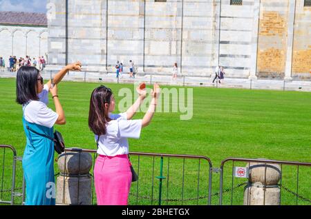 Pisa, Italien, 14. September 2018: Touristen Reisende asiatische chinesische, japanische weibliche Mädchen posieren, Spaß haben, stereotype Fotos machen, zeigen Größe, halten mit Fingern Schiefen Turm, Toskana Stockfoto