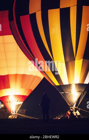 Nachts zeigen und starten Sie von Heißluftballons beleuchtet in der Dunkelheit, mit einem Fotografen im Vordergrund Stockfoto