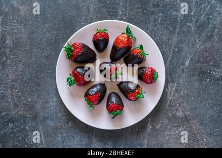 Draufsicht auf frische gesunde Erdbeeren, die in dunkle Schokolade auf einem Teller getaucht sind Stockfoto