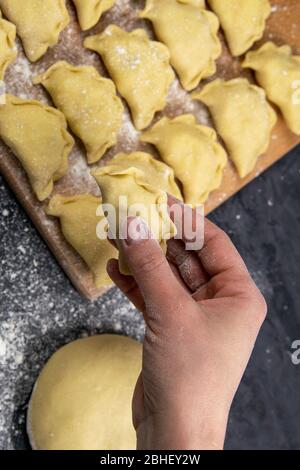 Knödel in Mehl auf dem Holzbrett, Hand halten varenik vor dem Kochen. Ukrainische traditionelle Küche Stockfoto