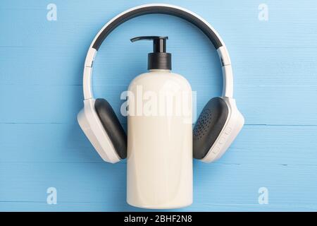 Kunststoff beige Gel Seifenbehälter mit Spender und weißen schwarzen kabellosen Kopfhörer auf einem hellblauen Holzhintergrund. Das Konzept des Coronavirus quar Stockfoto
