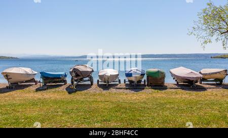 Segelboote an Land am Ufer des Ammersees (Ammersee). In einer Reihe aufgereiht. Die Boote sind mit Plane bedeckt. Panoramafarma. Stockfoto