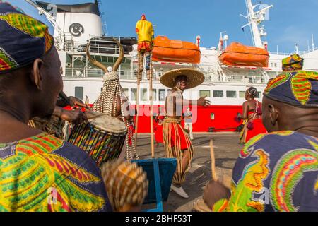 Kulturelle Performance mit Tänzern, einem Mann auf Stelzen und Musikern vor der MS Expedition im Hafen von Lomé, Togo. Stockfoto