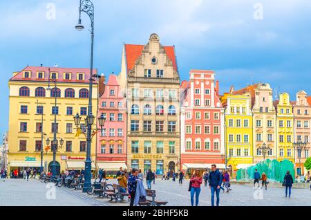 Breslau, Polen, 7. Mai 2019: Reihe von bunten traditionellen Gebäuden mit bunten Fassaden, Glasbrunnen und Spaziergänger auf dem Rynek Marktplatz in der Altstadt historischen Stadtzentrum Stockfoto