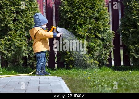 Kleiner Junge mit Gießkanne Bewässerung Bäume auf Hinterhof. Happy Kindheitkonzept Stockfoto