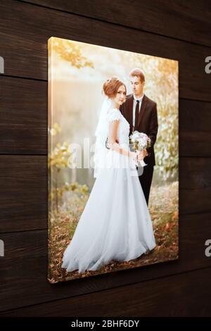 Fotoleinwand drucken. Beispiel für gestreckte Hochzeitsfotografie mit Galeriefolie, Seitenansicht. Brautporträt hängt an der braunen Holzwand Stockfoto